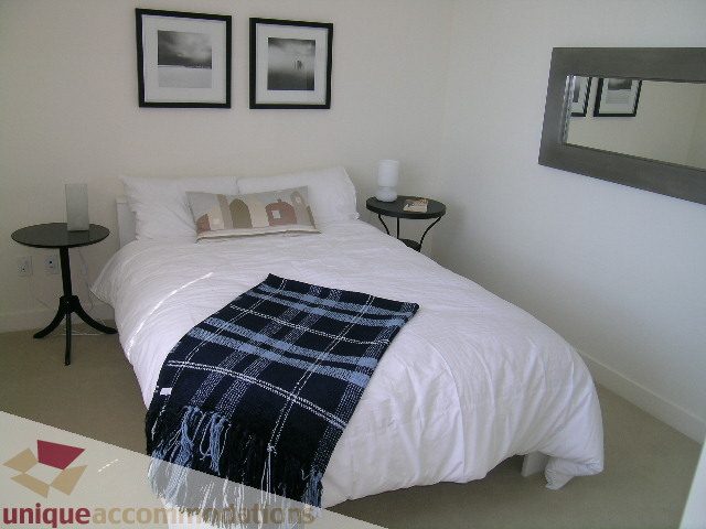 Spacious bedroom with a cozy bed, plaid throw, and minimalist decor, perfect for a comfortable stay. - 1204-1030 West Broadway, Vancouver West Side