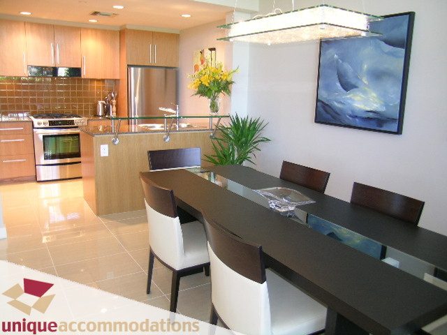 Modern kitchen with sleek countertops, stainless steel appliances, and a stylish dining area featuring a black table and...