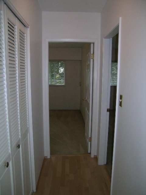 Bright hallway with hardwood floors and white walls, leading to a room with a window. - 147 - 3300 Capilano Rd, North Vancouver