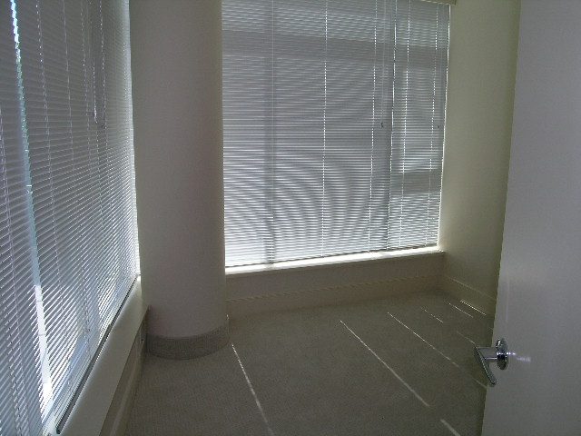 Bright living room with large windows and blinds, showcasing natural light and a clean, minimalist design.