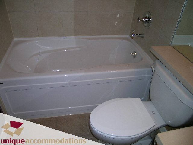Bathroom with white bathtub and toilet, beige tile walls. - 163 Aquarius Mews, Vancouver Downtown