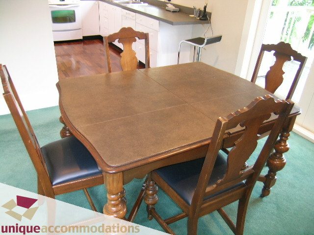 Bright dining area with wooden table and chairs, green carpet, and kitchen in the background. - 3447 West 1st Avenue, Vancouver West Side