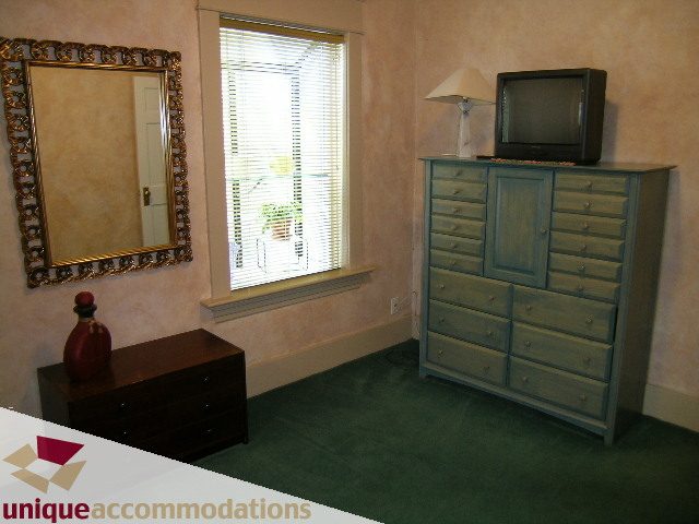 Bright bedroom with green carpet, dresser, mirror, and window with blinds. - 3447 West 1st Avenue, Vancouver West Side
