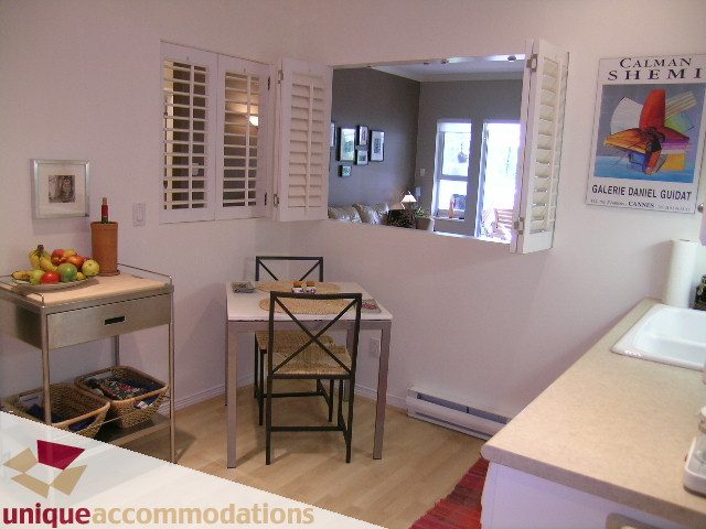 Bright kitchen with white countertops, hardwood floors, and open shutters leading to a cozy living area. - 304 - 1281 Parkgate Avenue, North Vancouver