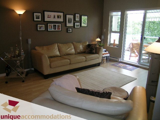Bright living room with leather sofa, hardwood floors, and large windows. - 304 - 1281 Parkgate Avenue, North Vancouver