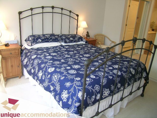 Bright bedroom with blue floral bedspread, wrought iron headboard, and wooden nightstands. - 304 - 1281 Parkgate Avenue, North Vancouver