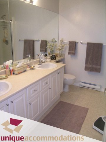 Furnished bathroom with white cabinets, beige countertops, and a large mirror. - 304 - 1281 Parkgate Avenue, North Vancouver