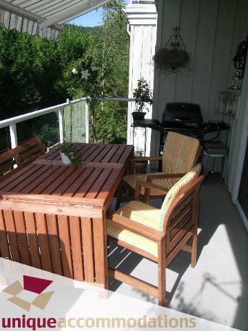 Furnished patio with wooden furniture and grill, surrounded by greenery. - 304 - 1281 Parkgate Avenue, North Vancouver
