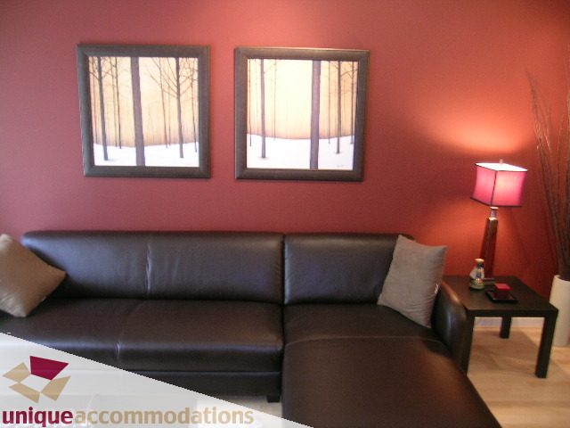 Spacious living room with a leather sectional, modern artwork, and a cozy corner lamp. - 105 - 530 Raven Woods, North Vancouver