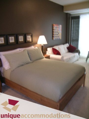 Spacious bedroom with wooden platform bed, neutral decor, and large window. - 105 - 530 Raven Woods, North Vancouver