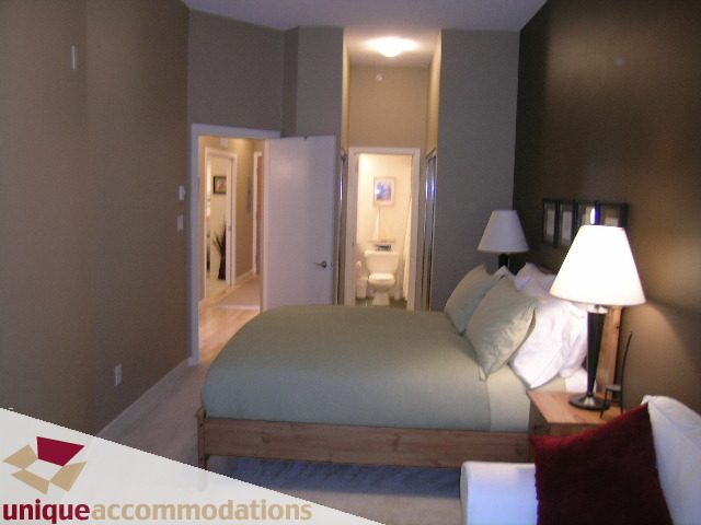 Spacious 1-bedroom + den condo with cozy bedding and modern decor, featuring a well-lit hallway and a comfortable bedroom...