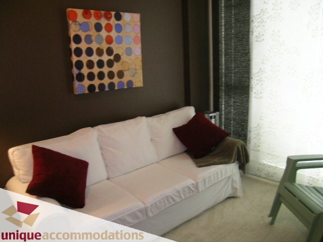 Spacious living room with modern decor, featuring a white sofa with red accents and a colorful abstract wall art.