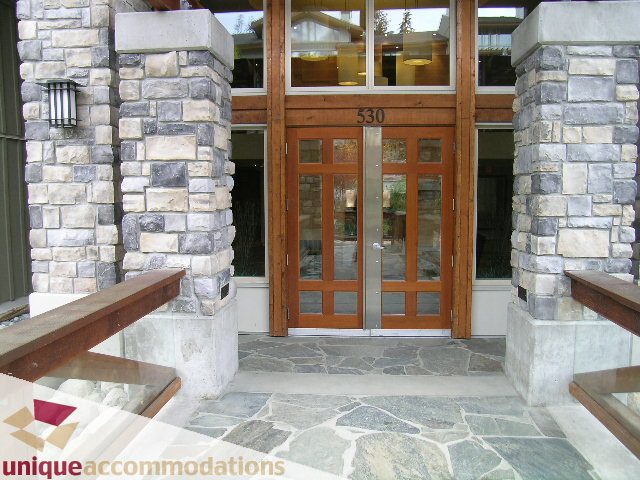 Furnished 1-bedroom + den condo with stone accents and wooden doors, perfect for cozy getaways. - 105 - 530 Raven Woods, North Vancouver