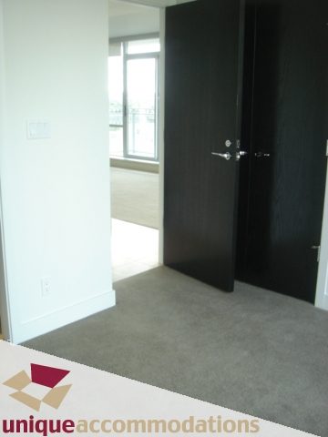Spacious living room with large windows and dark wood doors, offering a modern and cozy feel. - 1101 -1455 Howe Street, Vancouver Downtown