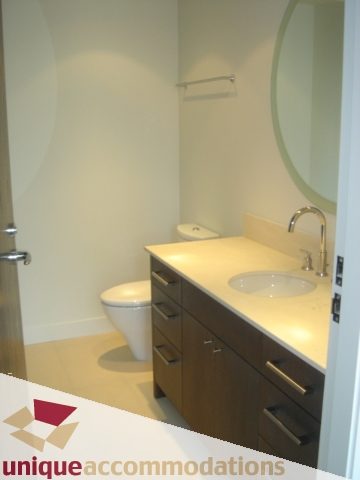 Modern bathroom with sleek white countertops and wooden cabinets. - 1101 -1455 Howe Street, Vancouver Downtown
