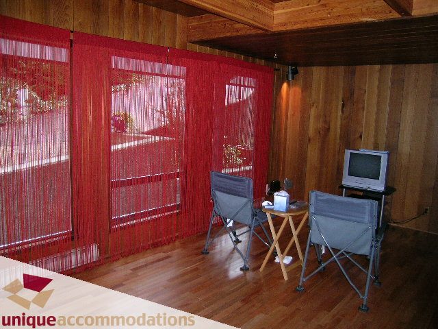 Furnished living room with red string curtains, hardwood floors, and a small TV setup. - 310 Bayview Road, West Vancouver