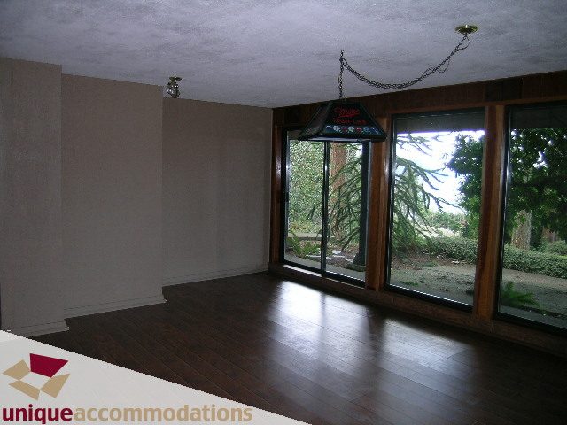 Bright living room with hardwood floors and large windows showing trees outside. - 310 Bayview Road, West Vancouver