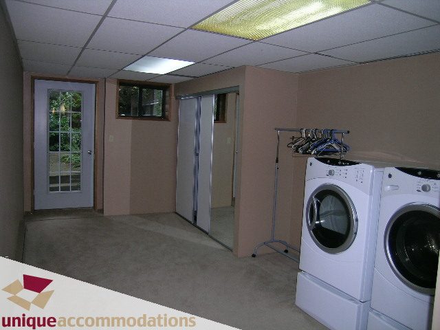 Laundry room with stacked washer and dryer, beige carpet, and closet doors. - 310 Bayview Road, West Vancouver