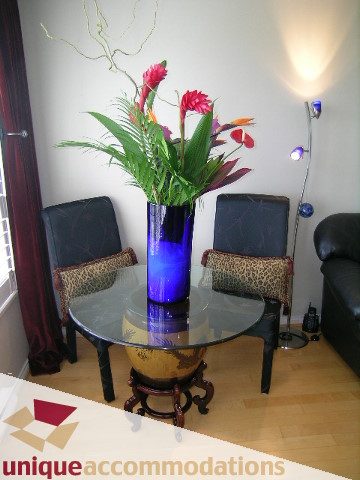 Living room with hardwood floors, a glass table, and a vibrant floral arrangement in a blue vase. - 2606-1189 Howe Street, Vancouver Downtown