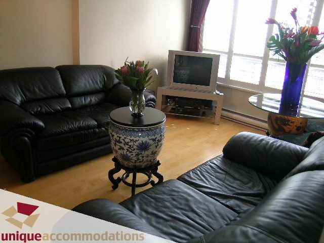 Bright living room with black leather couch, hardwood floors, and a cozy corner with a vase of flowers. - 2606-1189 Howe Street, Vancouver Downtown