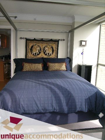 Bright bedroom with blue bedding, leopard print pillows, and a tapestry above the bed. - 2606-1189 Howe Street, Vancouver Downtown