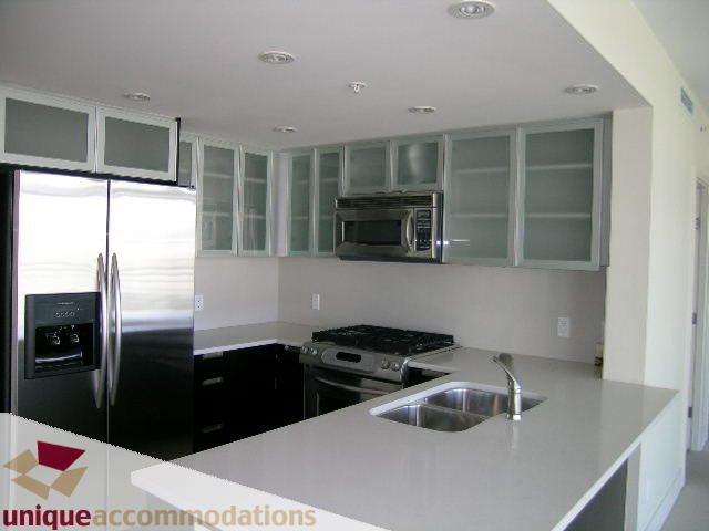 Bright kitchen with modern white countertops and stainless steel appliances, featuring a double sink and ample cabinet space.