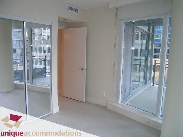 Bright living room with large windows offering a city view and sliding glass doors leading to a balcony. - 705 - 1205 W Hastings, Vancouver Downtown