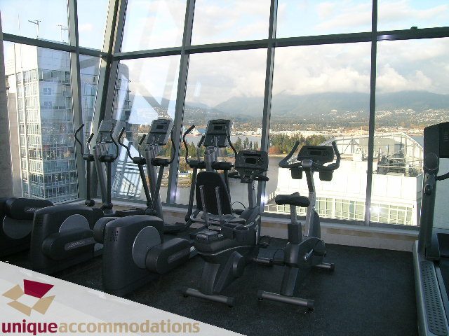 Furnished 1-bedroom condo with city view from large windows, gym equipment visible. - 705 - 1205 W Hastings, Vancouver Downtown