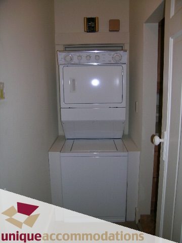 Bright laundry room with stacked washer and dryer, white cabinets. - 782 W 22nd Ave, Vancouver West Side