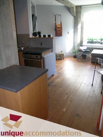 Bright kitchen with dark countertops and hardwood floors, leading into a cozy living area with a window view. - 211- 1216 Homer, Vancouver Downtown