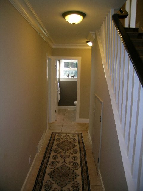 Narrow hallway leading to a bright, sunlit room with a patterned rug and white railings. - 3554 St. Andrews Avenue, North Vancouver