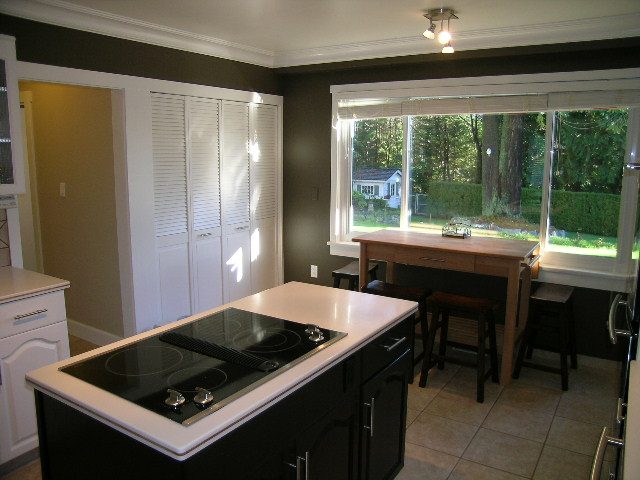 Bright kitchen with white countertops and black cabinets, leading to a dining area with a sliding glass door to the garden.
