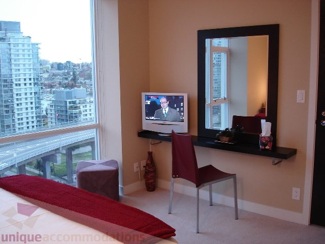 Bright bedroom with city view and large mirror, furnished with red accents. - 1504 - 1455 Howe Street, Vancouver Downtown