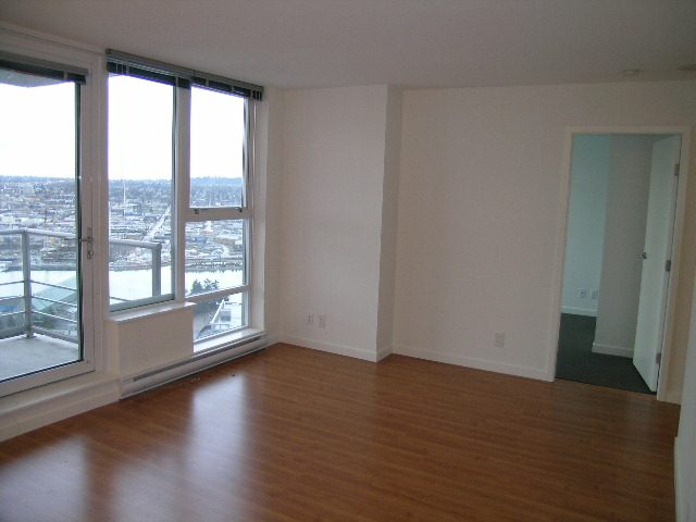 Spacious living room with hardwood floors, large windows offering a city view, and a sliding glass door leading to a balcony.