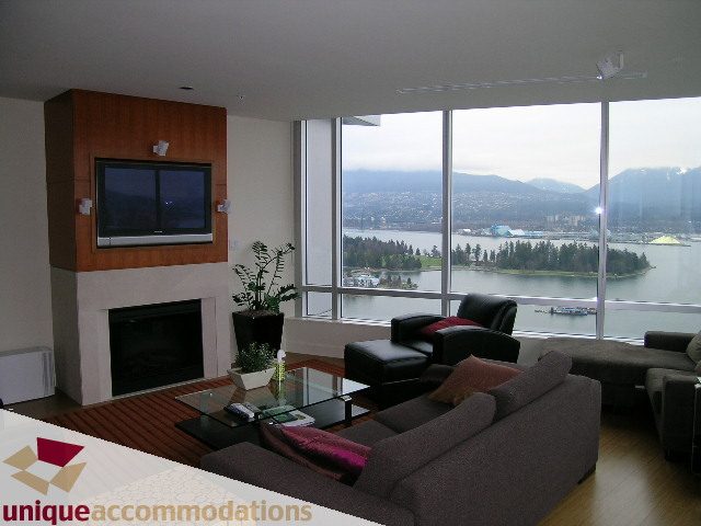 Living room with large windows offering a stunning city view, modern furniture, and a flat-screen TV mounted on a...