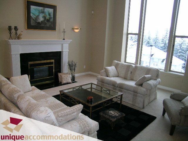 Furnished living room with large windows, cozy seating, and a fireplace. - 4139 Quarry Court, North Vancouver