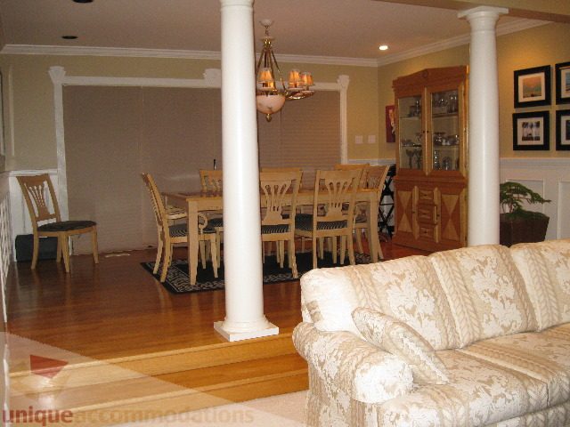 Furnished living room with patterned couch and dining area with wooden table and chairs. - 4139 Quarry Court, North Vancouver
