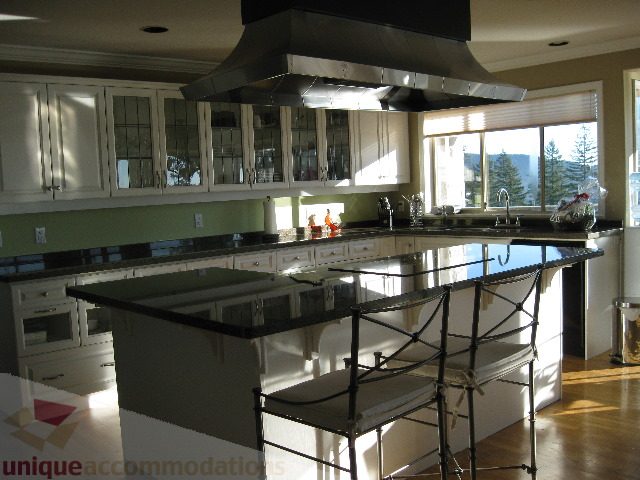Bright kitchen with black countertops, hardwood floors, and a city view. - 4139 Quarry Court, North Vancouver