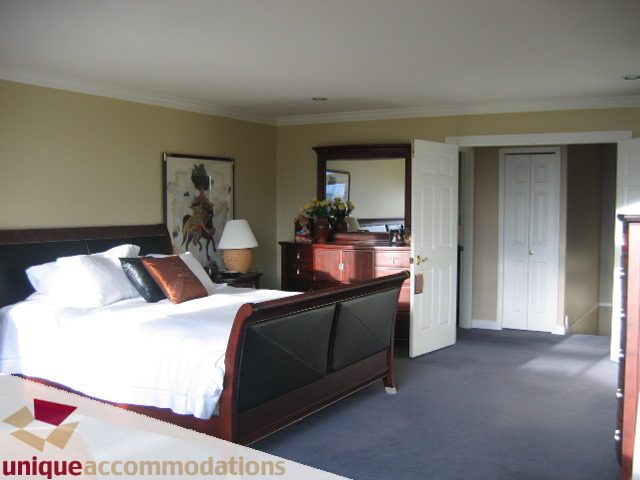 Spacious bedroom with large bed, wooden headboard, and mirrored closet. - 4139 Quarry Court, North Vancouver