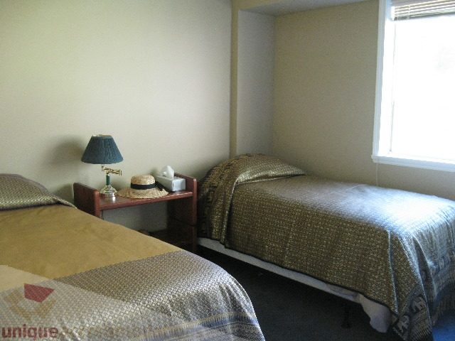 Furnished bedroom with patterned bedding and a small table with a lamp. - 4139 Quarry Court, North Vancouver