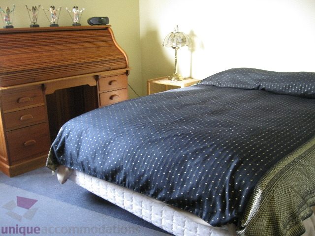 Furnished bedroom with dark blue bedding and wooden desk. - 4139 Quarry Court, North Vancouver