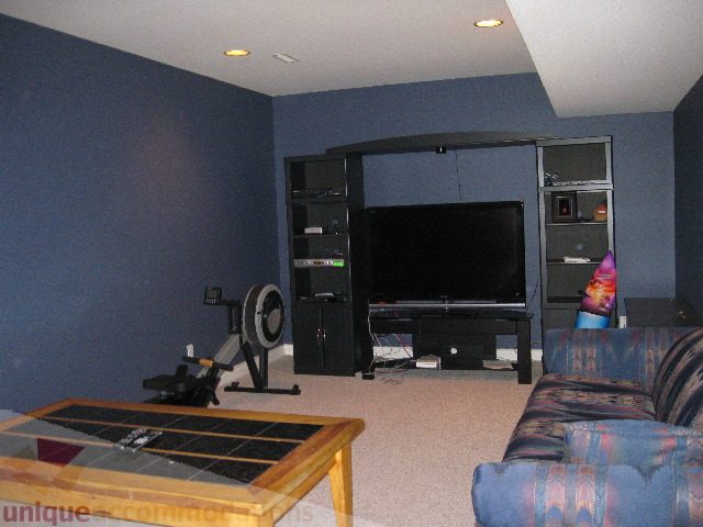 Living room with dark blue walls, a large TV, and a patterned couch. - 4139 Quarry Court, North Vancouver