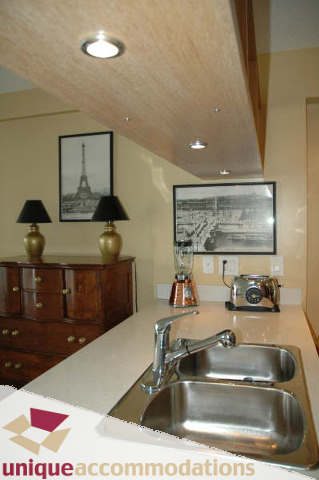 Bright kitchen with stainless steel double sink, wooden cabinets, and framed cityscape art. - 2314 - 938 Smithe Street, Vancouver Downtown