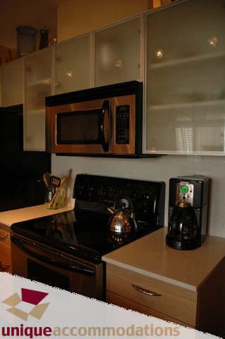 Bright kitchen with stainless steel appliances, light wood cabinets, and a black stove. - 2314 - 938 Smithe Street, Vancouver Downtown