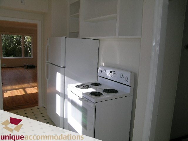 Bright kitchen with white appliances, hardwood floors, and open shelving. - 1428 29th Street, West Vancouver