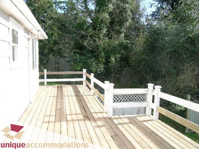Bright deck with wooden flooring and white railings, surrounded by lush greenery. - 1428 29th Street, West Vancouver