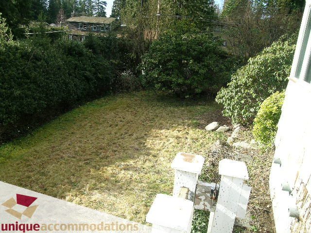 Fenced backyard with grass and shrubs, view of trees and houses in the distance. - 1428 29th Street, West Vancouver