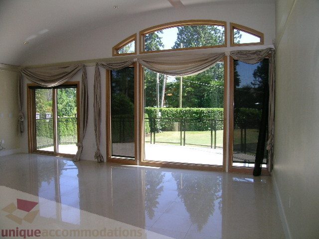 Spacious living room with large windows, hardwood floors, and a view of greenery. - 4215 Evergreen Ave, West Vancouver