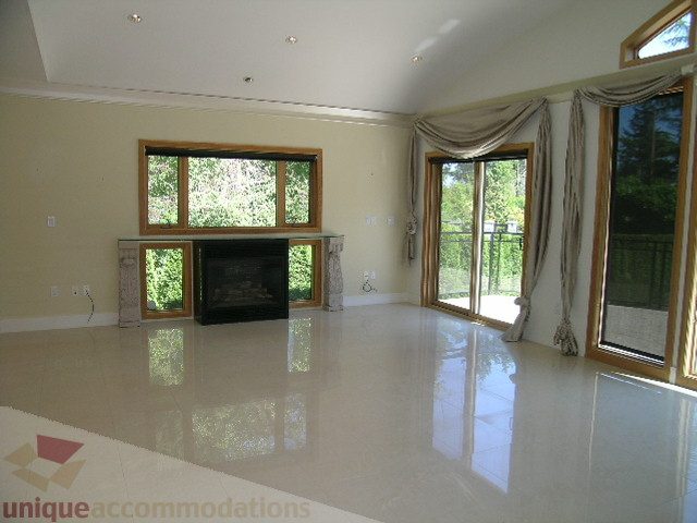 Bright living room with glossy floor, large windows, and fireplace. - 4215 Evergreen Ave, West Vancouver