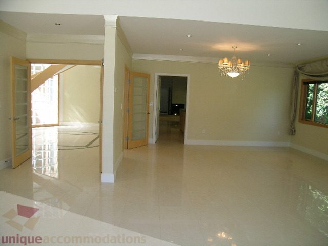 Bright living room with glossy tile floors and a chandelier, leading to a kitchen. - 4215 Evergreen Ave, West Vancouver